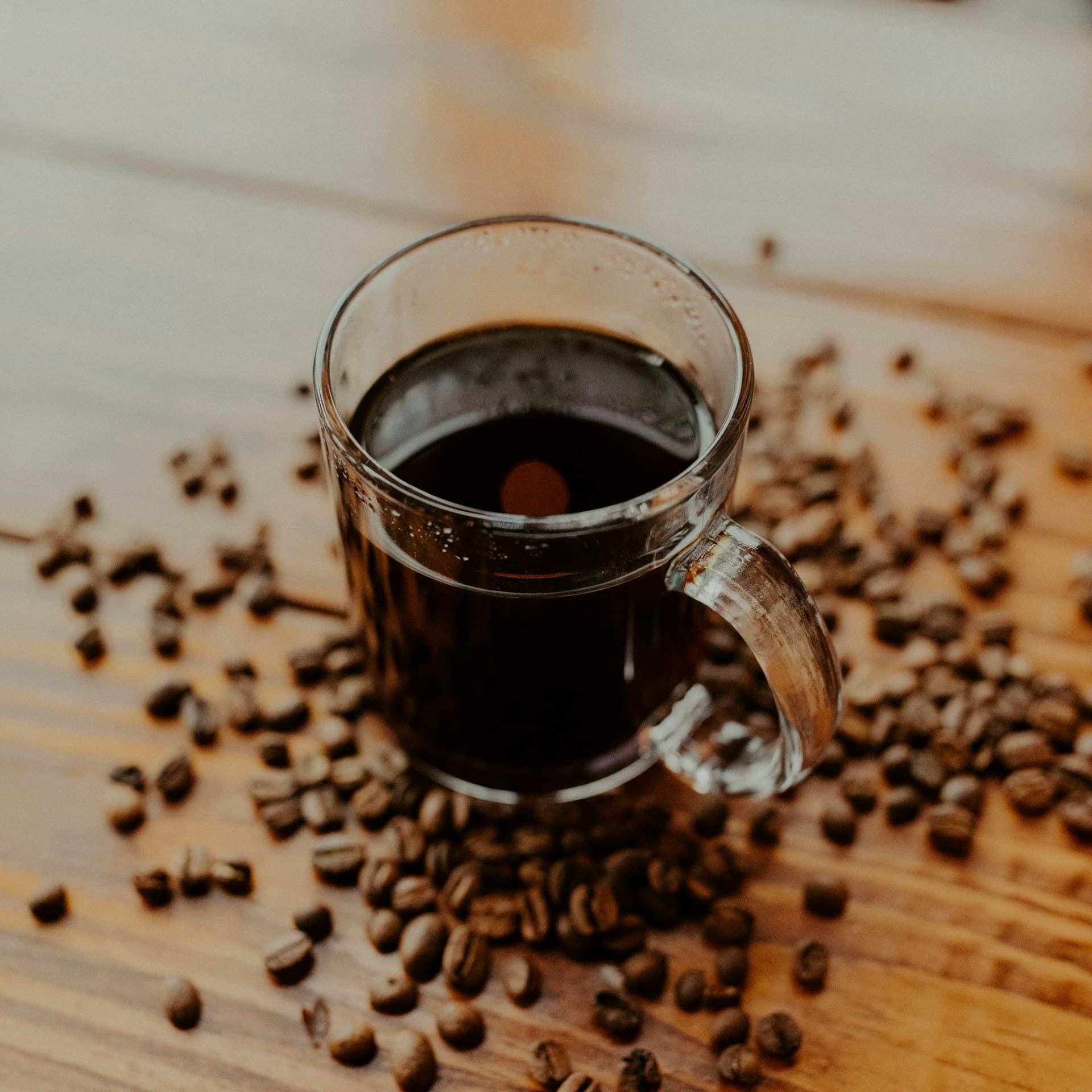 Una taza de café servida sobre una mesa de madera, con granos alrededor